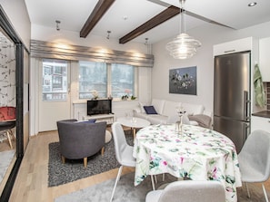 A modern living room with a sofa, a dining table with floral tablecloth, a grey armchair, and a kitchen area with a refrigerator. - Kelotähti a 11 by Interhome (Inari)