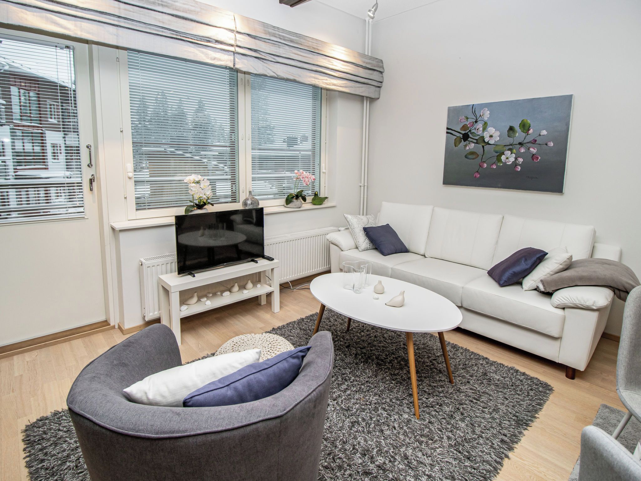 Una sala moderna con un sofá, un sillón gris, una mesa de centro y un televisor sobre un soporte blanco.