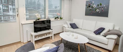 Una sala moderna con un sofá, un sillón gris, una mesa de centro y un televisor sobre un soporte blanco.