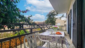 Ein Balkon mit Tisch für zwei Personen, einem Stuhl und Blick auf einen Garten sowie Gebäude im Hintergrund.