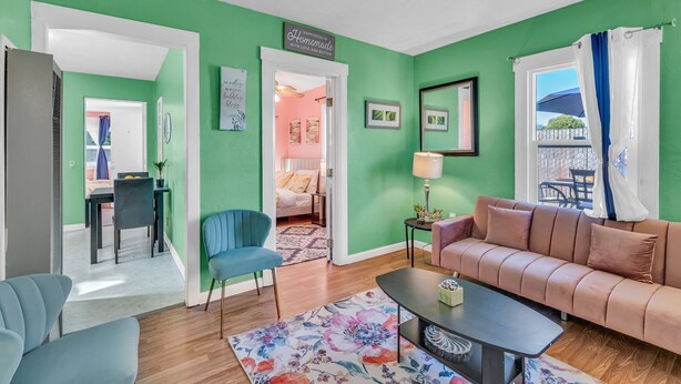 Un salon avec un mur vert, un canapé, une table basse et un coin repas comprenant une table et des chaises.