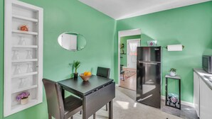 Une cuisine avec un réfrigérateur noir, une table à manger avec des chaises et un meuble blanc avec des étagères.