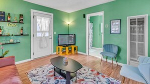 Un salon avec un téléviseur posé sur un meuble jaune, un tapis à motifs floraux et un mur vert.