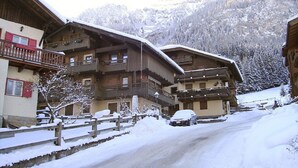 Un poble de muntanya cobert de neu amb edificis de fusta, una tanca de fusta i un cotxe estacionat a una carretera amb neu.