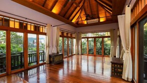 A spacious room with large sliding glass doors, wooden flooring, ceiling fans, and a view of greenery outside. - Eden Pool Villa  (Rawai)