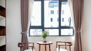 Une pièce avec une grande fenêtre, deux chaises en bois, une petite table ronde et une plante en pot.