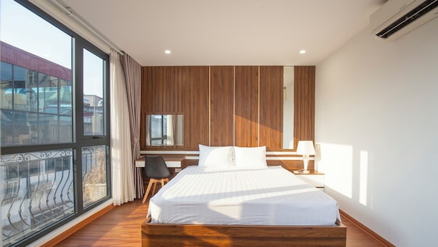 Une chambre moderne avec un grand lit, des murs recouverts de panneaux en bois, un bureau et une vue dégagée sur l’extérieur grâce à une grande fenêtre.