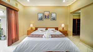 A hotel room with a large bed, two bedside tables with lamps, a wooden headboard, and three framed pictures on the wall. - Shana Homestay by EPS (Ubud)