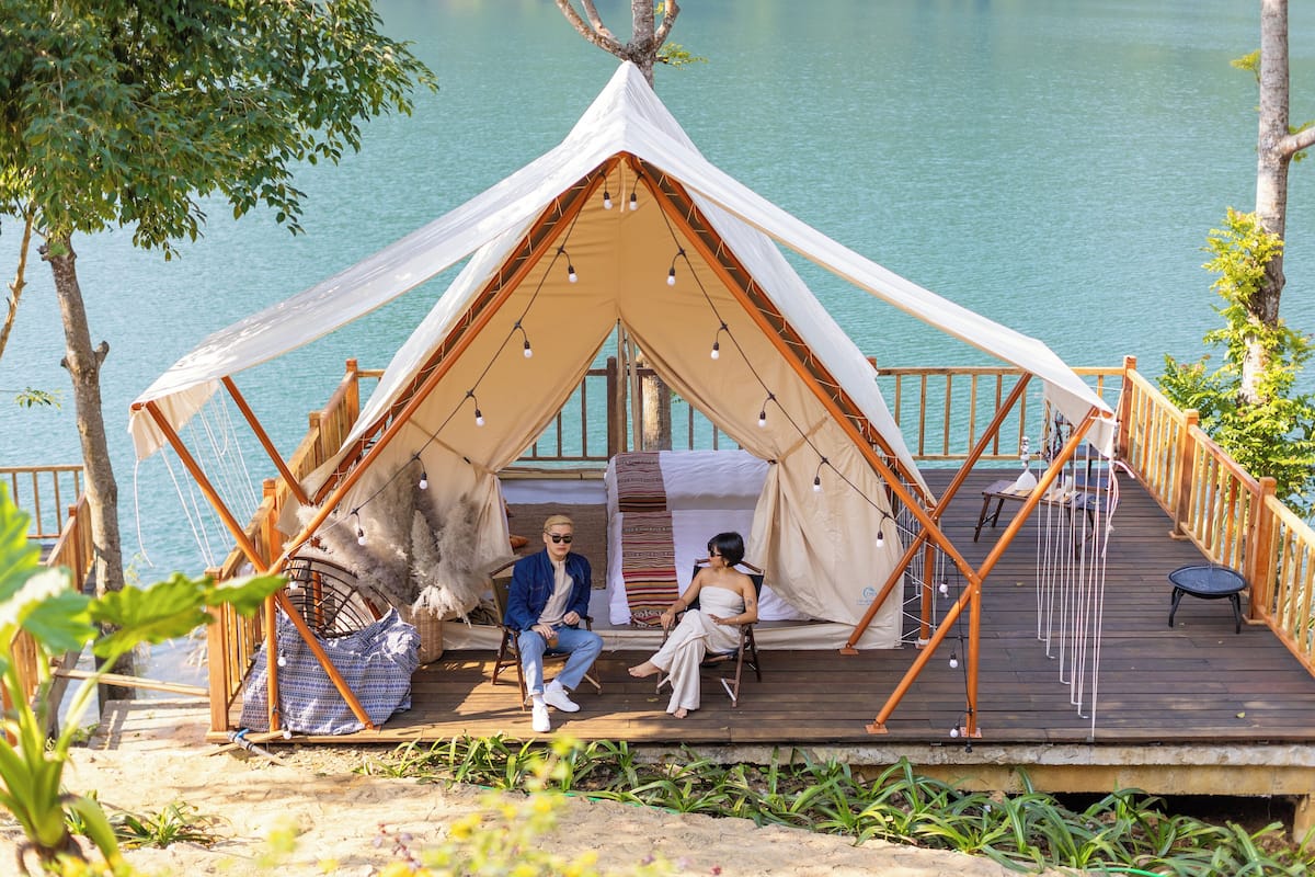 A tented accommodation by a lake with a wooden deck and a rope railing.