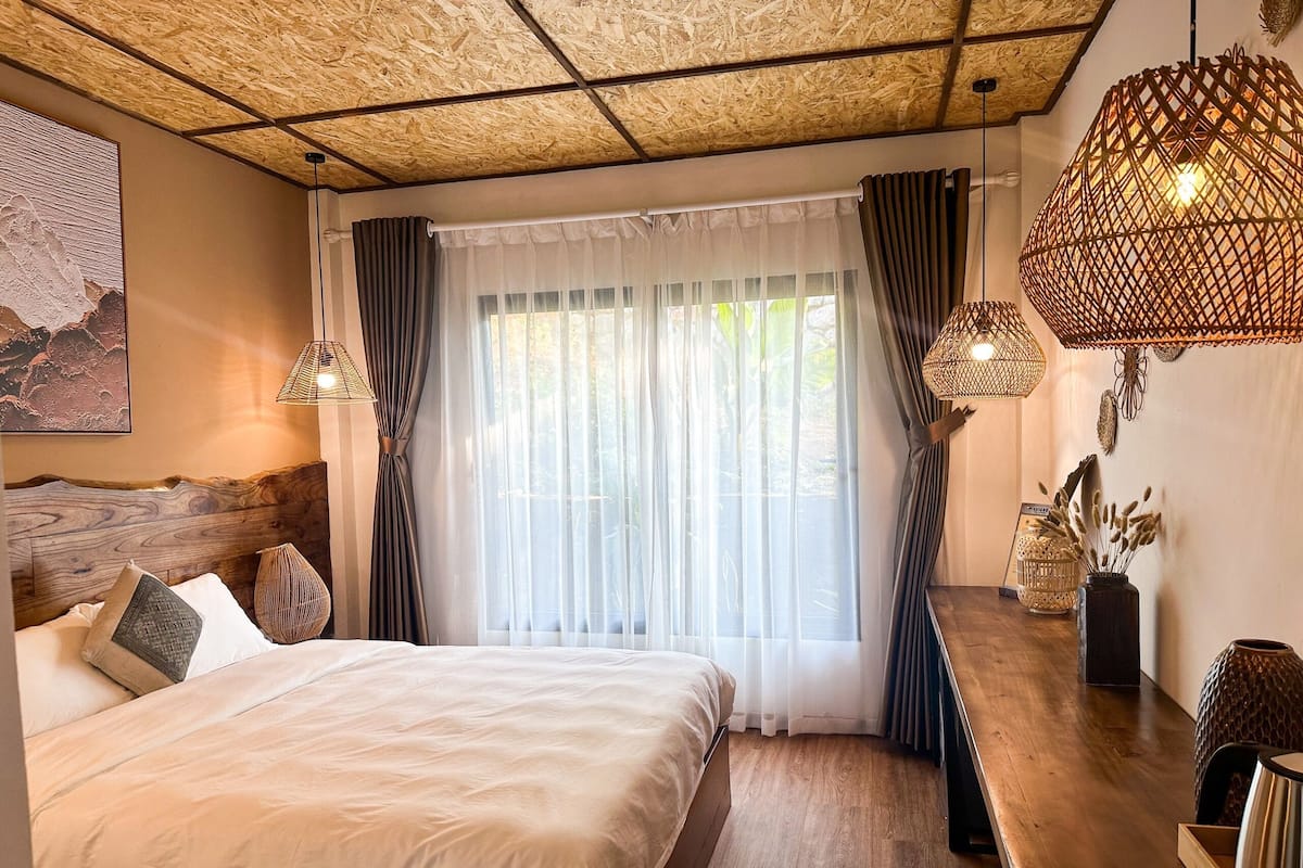 A bedroom with a large bed, wooden headboard, and a view of greenery outside.