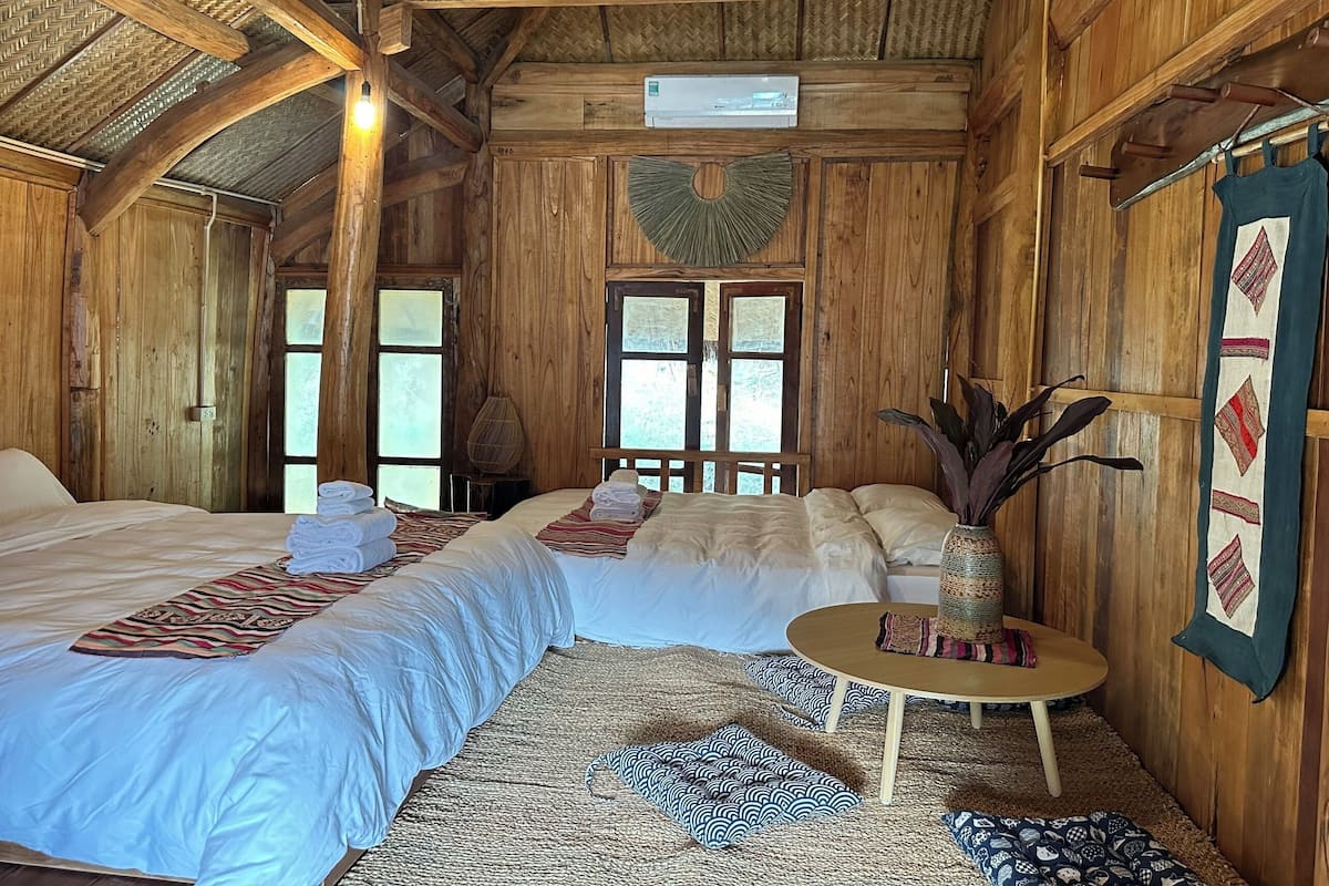 A wooden room with two beds, a small table, and a decorative plant.