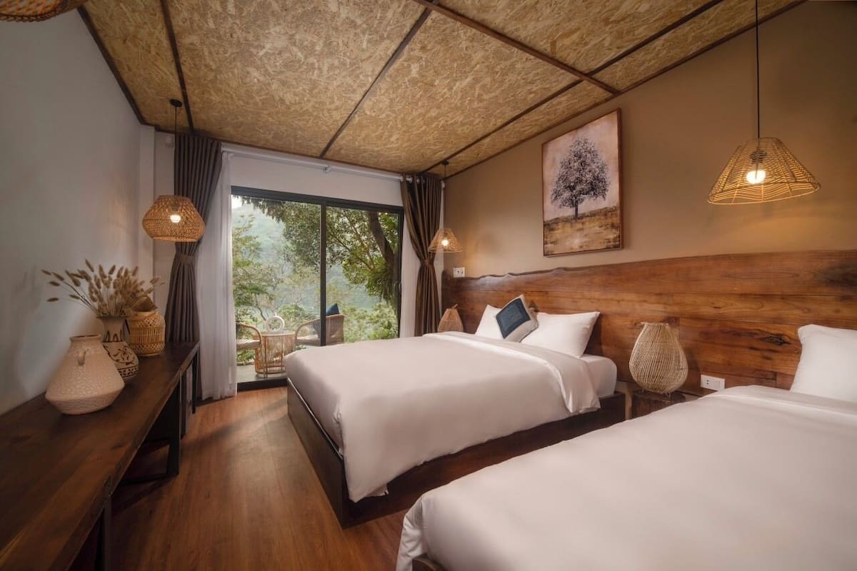 A hotel room with two beds, a wooden headboard, a large window with a view, and a ceiling with a textured pattern.