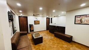 A spacious living room with a brown leather sofa, a glass coffee table, and a marble reception desk. - Nirvana inn (Prayagraj)