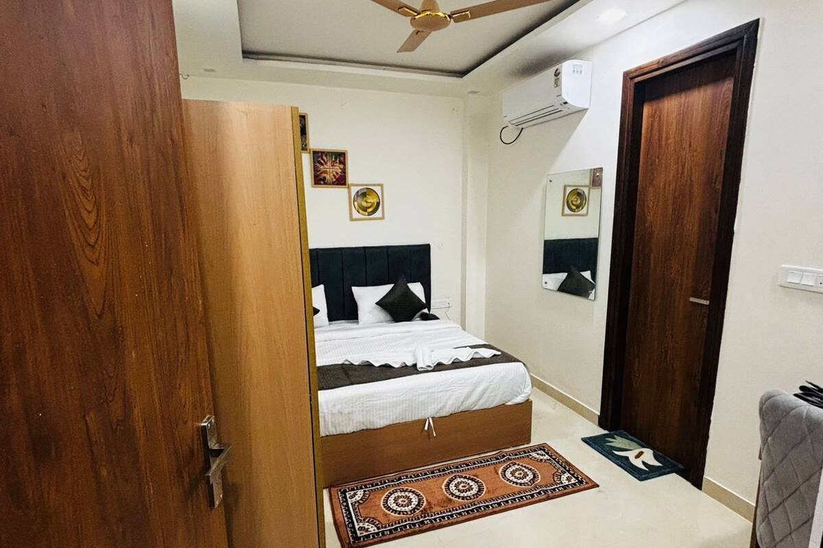 A bedroom with a bed, a ceiling fan, a wooden wardrobe, a door, and a small rug.