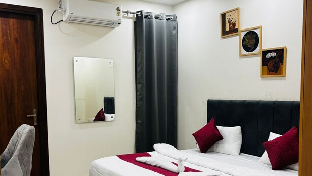 A neatly arranged bedroom with a bed, a chair, a mirror, and a ceiling fan. - Nirvana inn (Prayagraj)