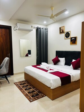 A neatly arranged bedroom with a bed, a chair, a mirror, and a ceiling fan. - Nirvana inn (Prayagraj)
