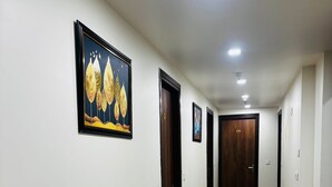 A long, narrow hallway with white walls and a polished tile floor. There are several doors along the hallway, some with visible handles. A framed picture hangs on the wall to the left. - Nirvana inn (Prayagraj)