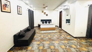 A bedroom with a bed, a sofa, a ceiling fan, and patterned floor tiles. - Nirvana inn (Prayagraj)