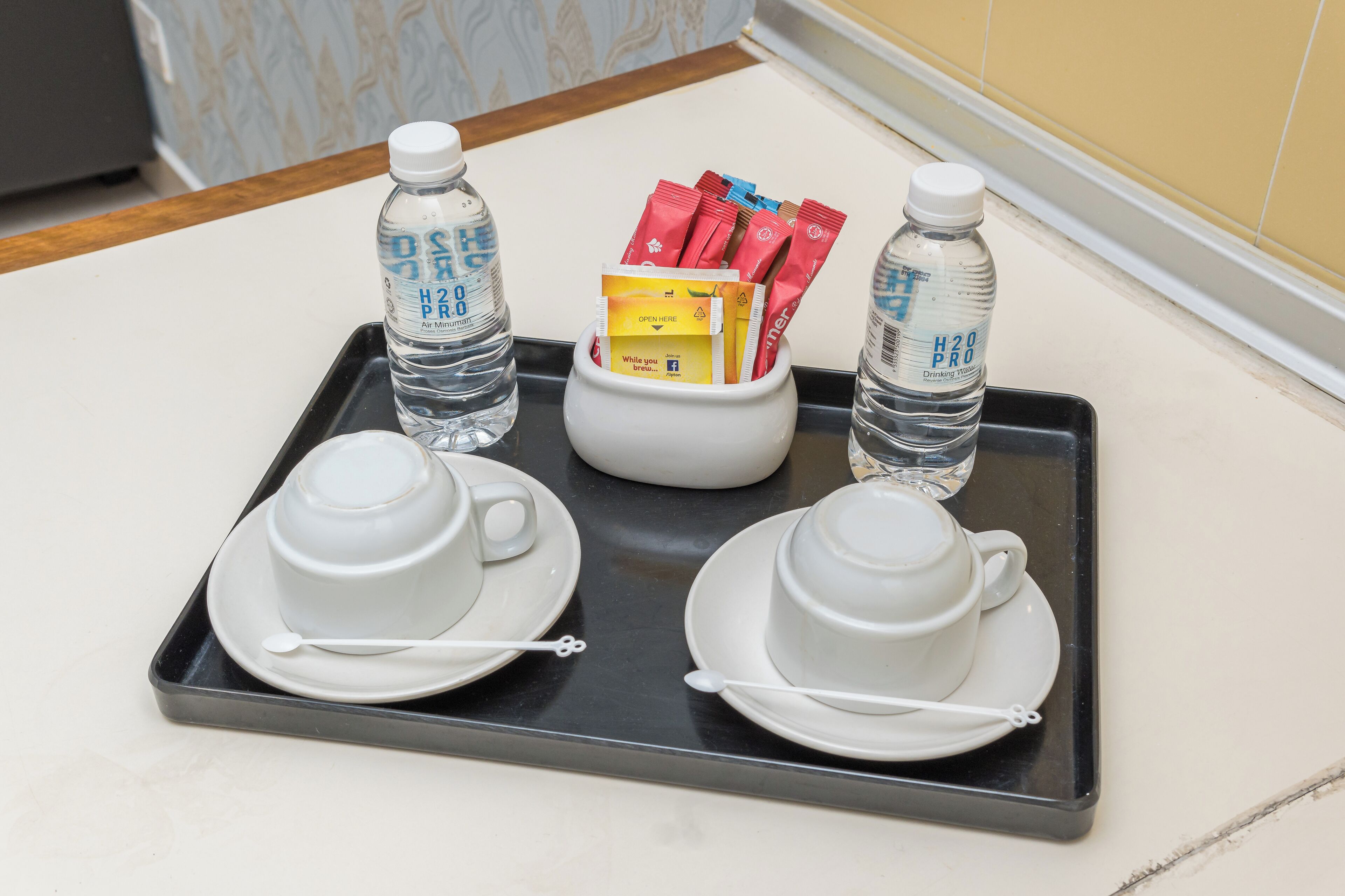 A tray with two white cups and saucers, two water bottles, and a small container holding red packets and a yellow card.
