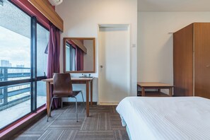 Een hotelkamer met een bed, een bureau, een stoel en een groot raam met uitzicht op de stad.