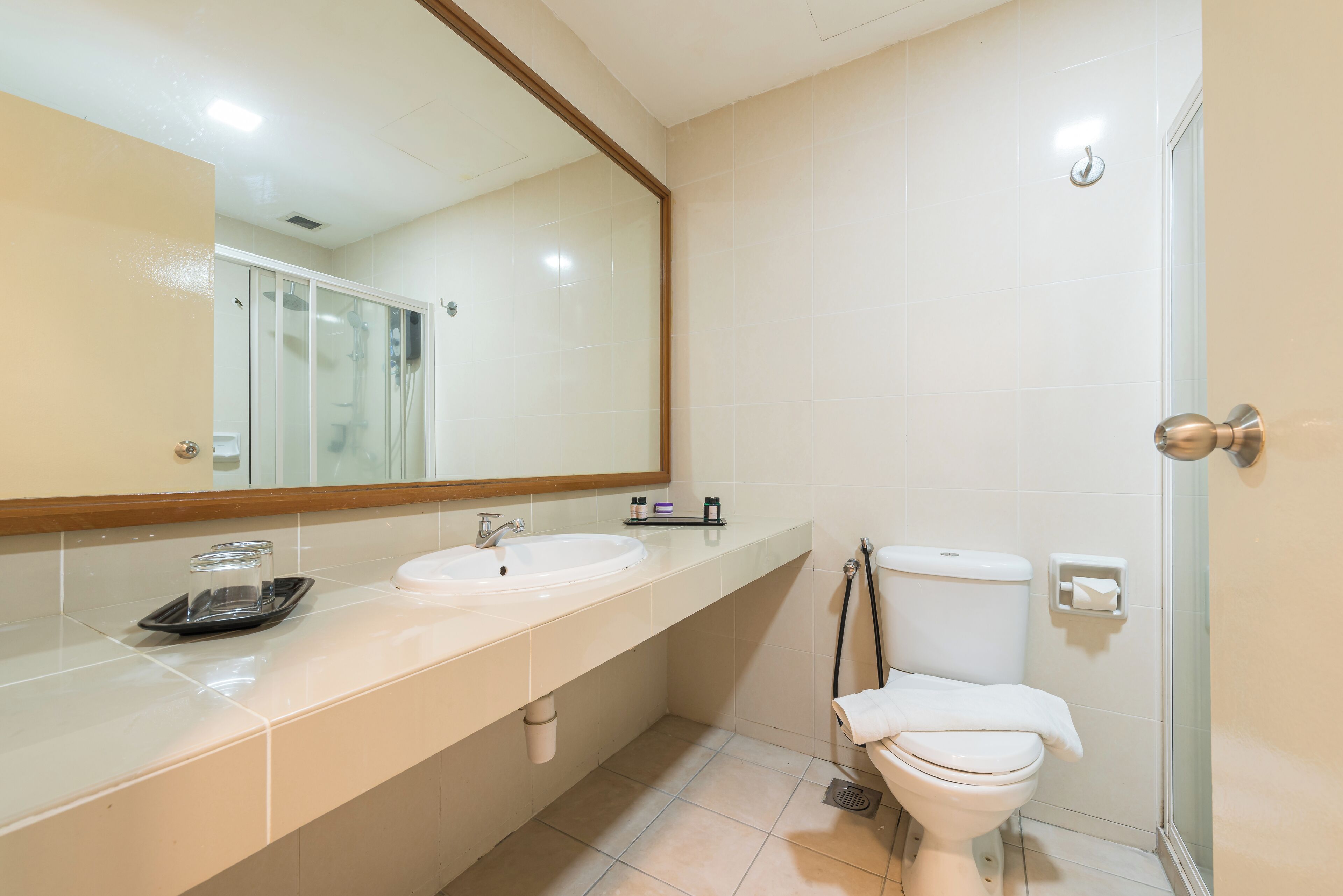 A modern bathroom with a large mirror, two sinks, a toilet, and a shower area.