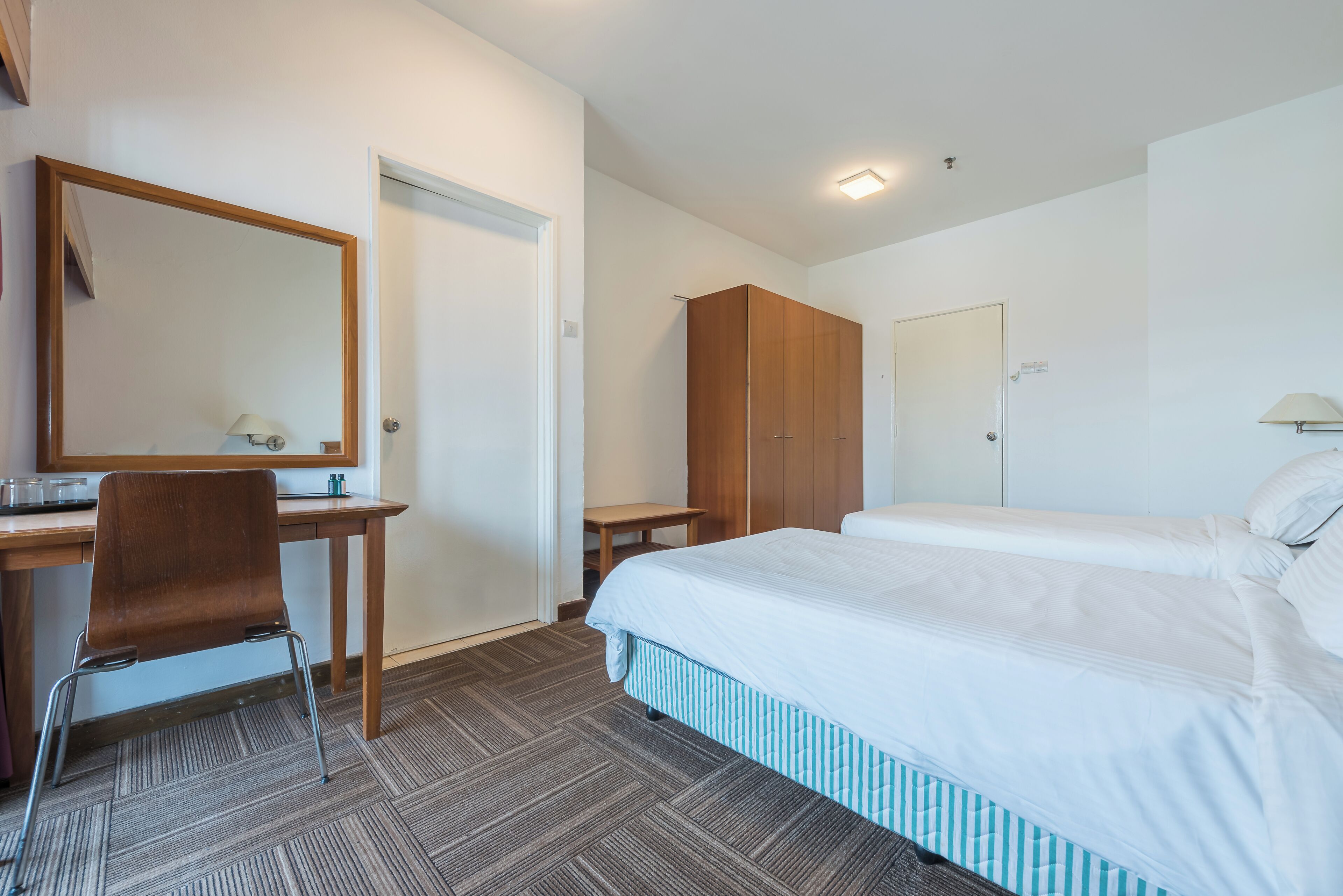 A hotel room with a bed, a desk, a chair, a wardrobe, and a mirror.