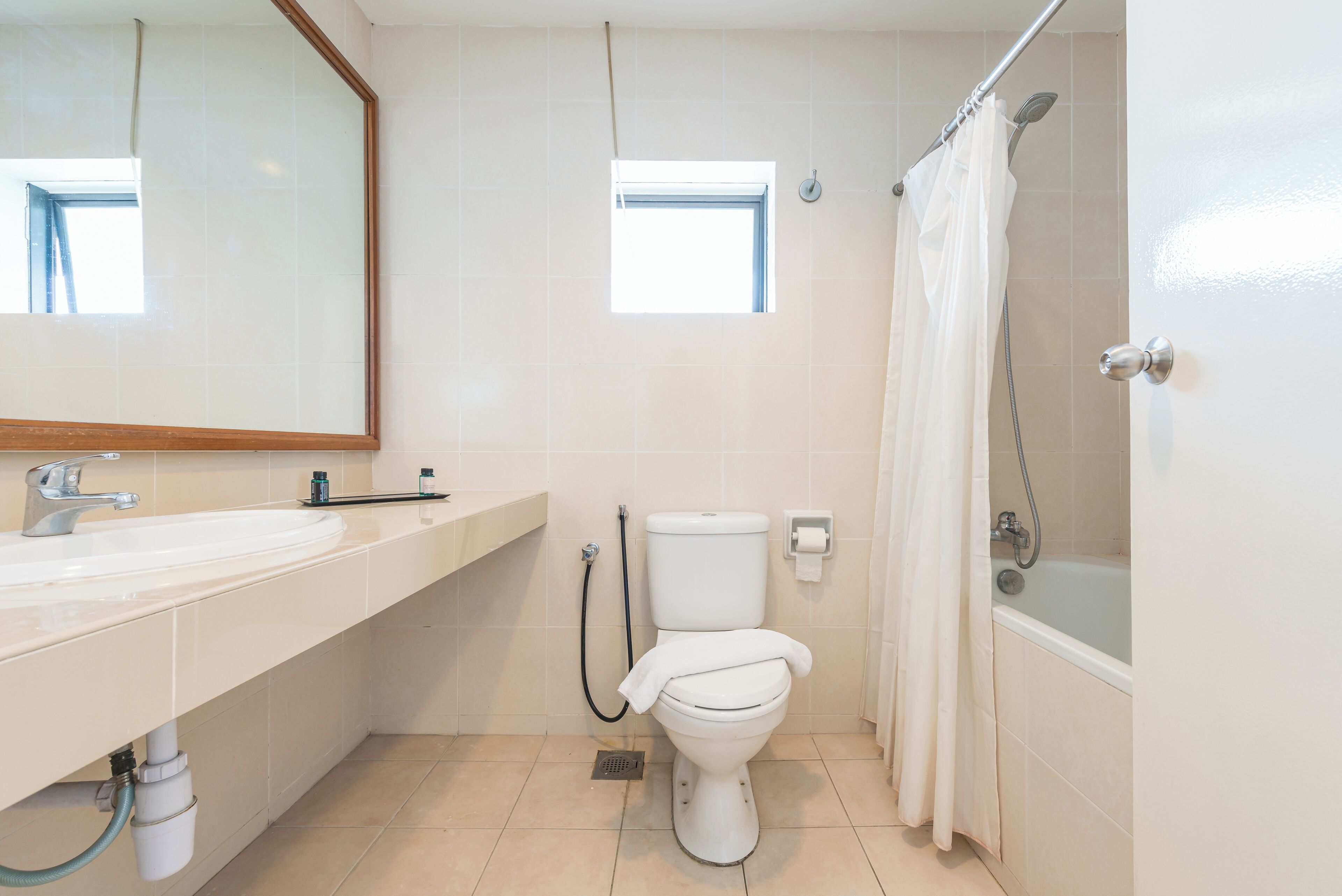 A bathroom with a toilet, sink, shower, and a small window.