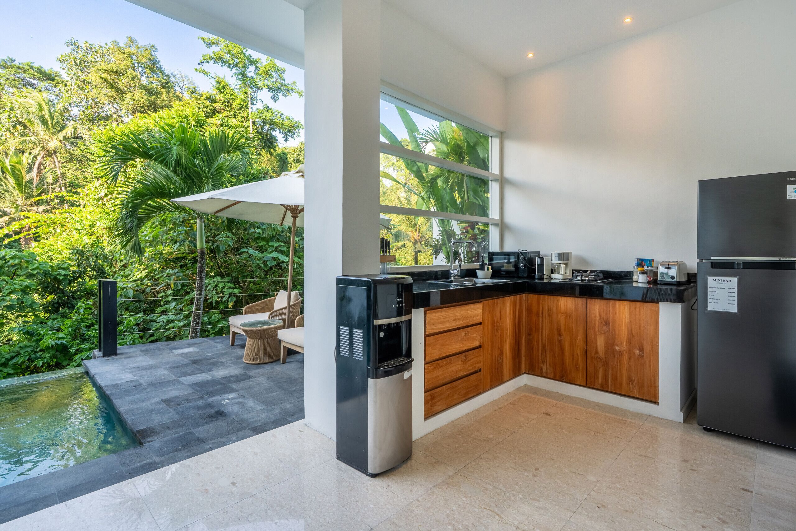 A modern kitchen with a built-in island, a refrigerator, and a view of lush greenery.