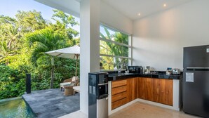 A modern kitchen with a built-in island, a refrigerator, and a view of lush greenery.