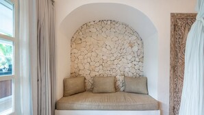A room with a stone wall, a cushioned bench, and a patterned door.