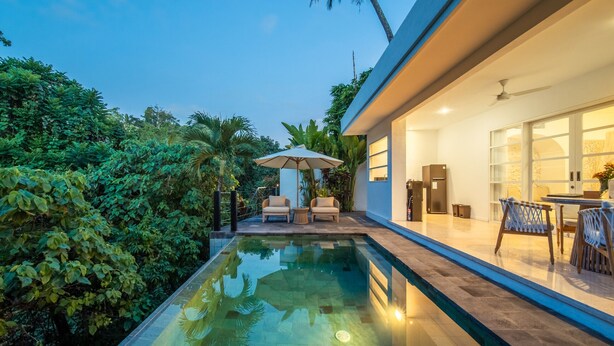 A modern house with a swimming pool, outdoor furniture, and a well-lit interior.