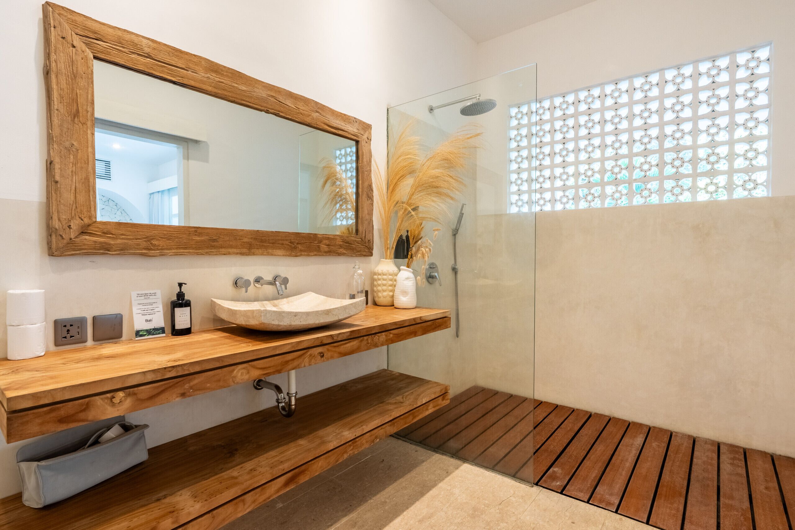 A modern bathroom with a wooden vanity, a large mirror, a glass shower enclosure, and a decorative window with a geometric pattern.