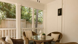 A covered patio with wicker furniture, a ceiling fan, and a view of a wooden fence and trees.