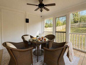 A covered patio with wicker chairs, a table with food and drinks, and a ceiling fan.