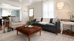 A living room with a sofa, armchair, coffee table, and a dining area in the background.