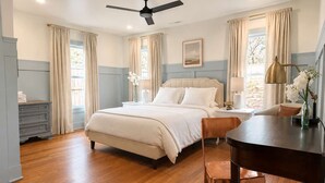 A bedroom with a bed, a desk, a chair, a ceiling fan, and a window with curtains.