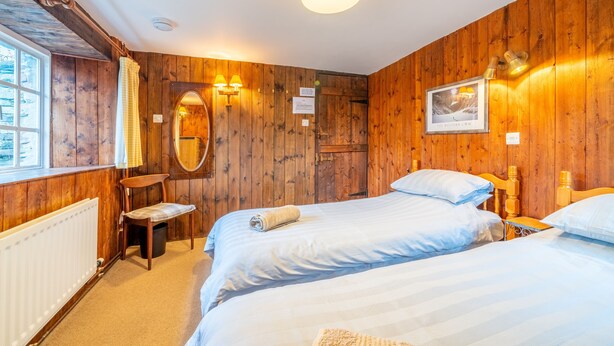 Une pièce chaleureuse en bois, avec deux lits, un banc, un radiateur et une fenêtre.
