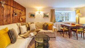 Una sala de estar acogedora con una pared de madera, un sofá con cojines, una mesa de centro de cristal y una mesa de comedor con sillas.