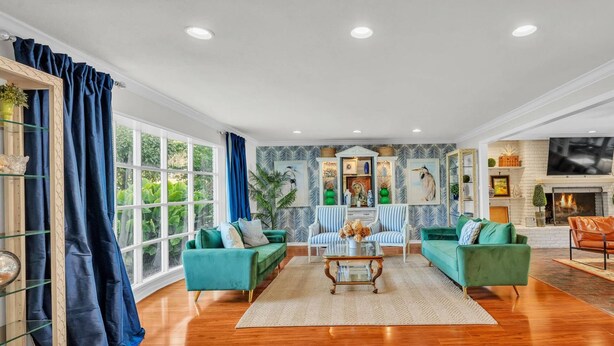 Ein geräumiges Wohnzimmer mit Holzboden, zwei grünen Sofas, einem Couchtisch und einem Kamin.
