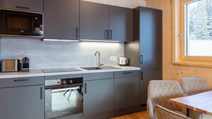 A modern kitchen with grey cabinets, a built-in oven, and a window with a view of trees.