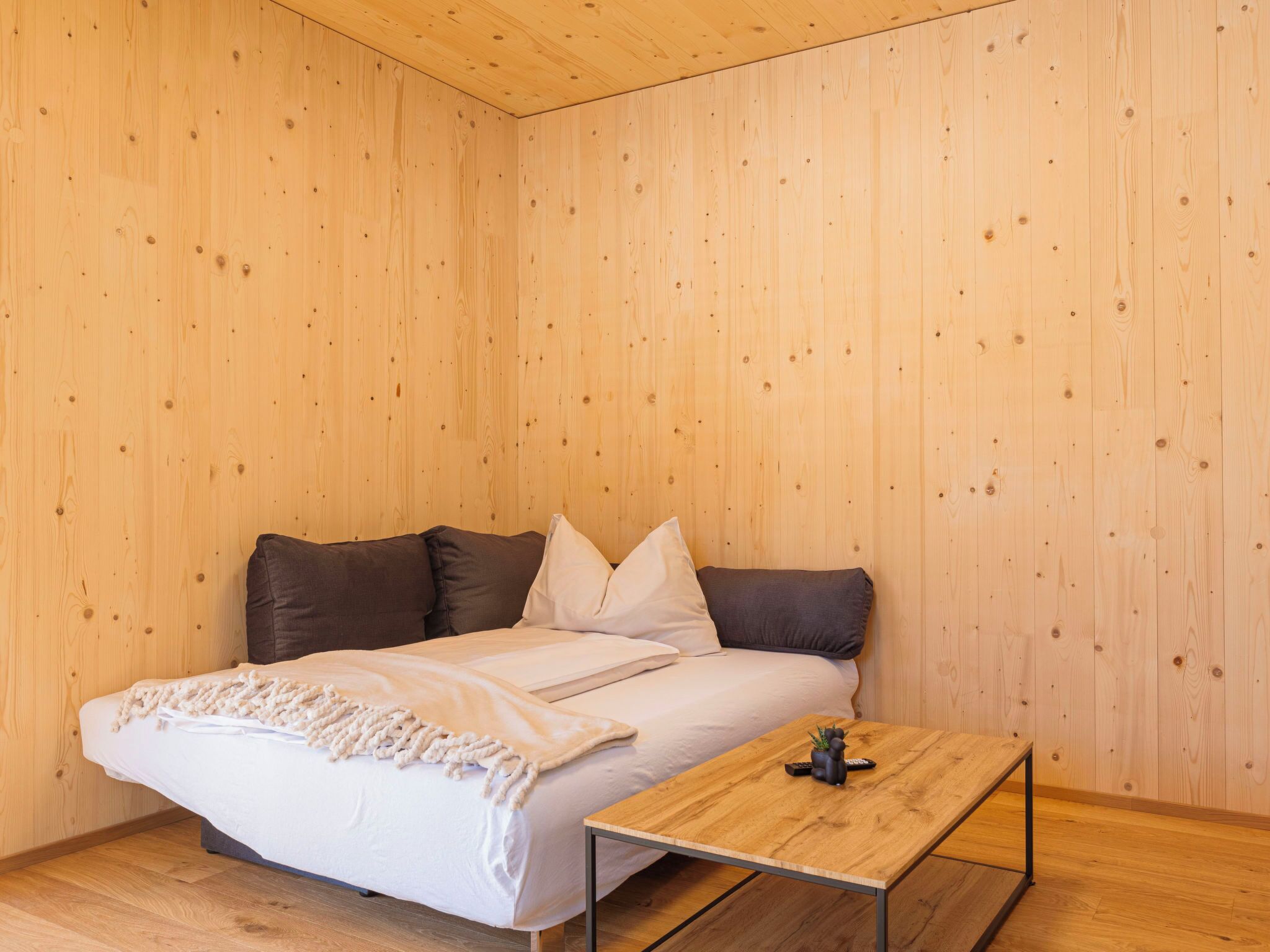 A bedroom with a bed, pillows, a bedside table, and a wooden floor.