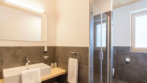 A modern bathroom with a large mirror, a sink with a vanity, a shower with glass doors, and a window providing natural light.