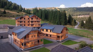 Un moderno edificio de madera con varios balcones, rodeado de un paisaje montañoso y un cielo despejado.