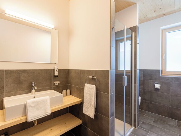 A modern bathroom with a large mirror, a sink with a vanity, a shower with glass doors, and a window providing natural light.