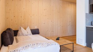 Un dormitorio moderno con techo de madera, una cama con ropa de cama blanca y una mesita con una planta.