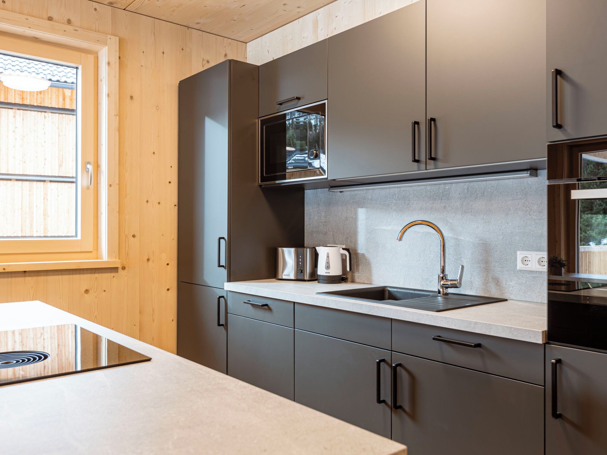 A modern kitchen with grey cabinets, a stainless steel sink, and a built-in microwave.