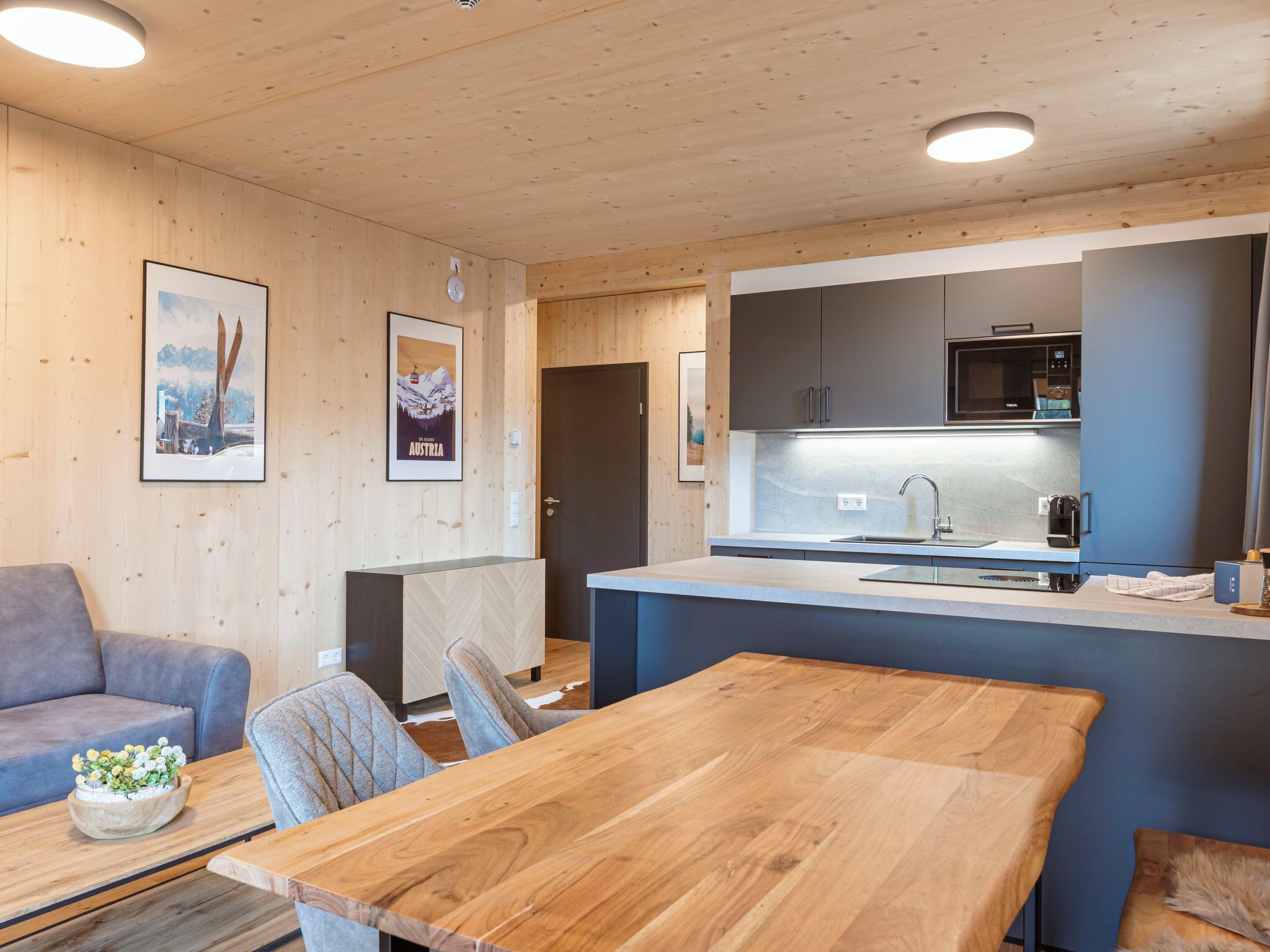 Eine moderne Küche mit Mikrowelle, Spüle und Kaffeemaschine. Im Wohnbereich befindet sich ein Holztisch mit Stühlen sowie eine Couch.