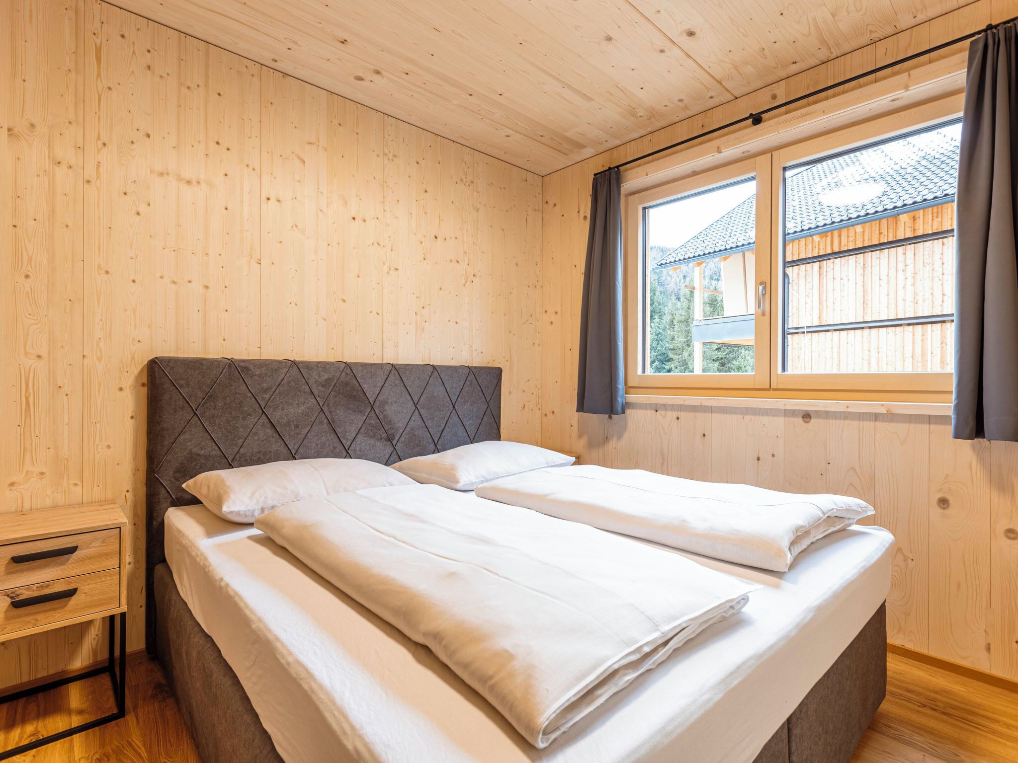 A wooden-paneled room with a bed, a nightstand, and a window with curtains.