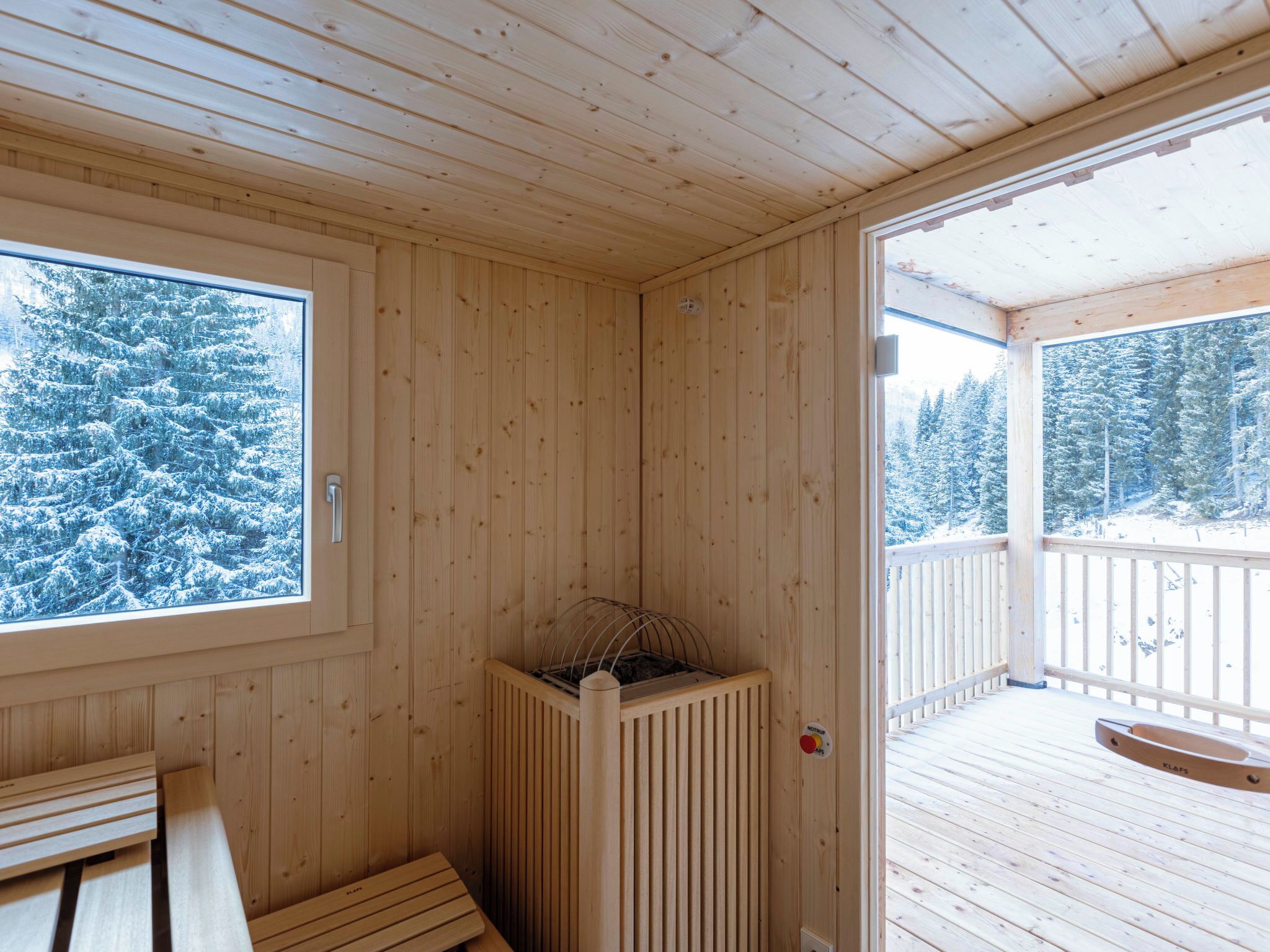 Un sauna en bois, avec un banc, un radiateur et une vue sur des arbres couverts de neige.