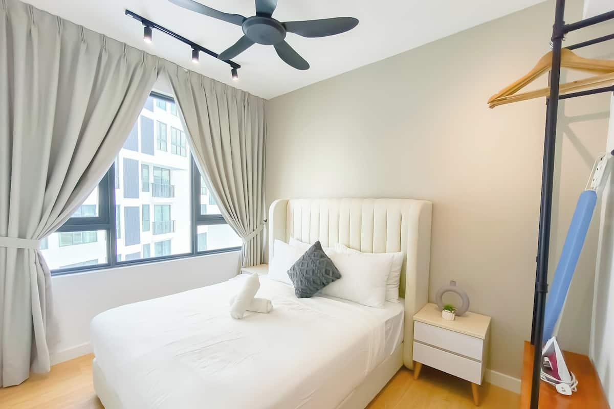 Una habitación de hotel con una cama, una mesita de noche, un ventilador de techo y una ventana con cortinas.